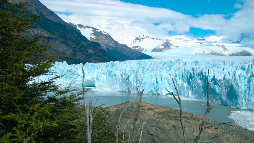 Perito Moreno Glacier in Argentina showcases massive ice formations descending into Lago Argentino, surrounded by mountains and sparse vegetation.