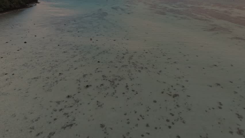 Drone clip zooming in while gaining elevation over tranquil shallow waters and distant limestone cliffs during sunset in Phi Phi Islands, Thailand.