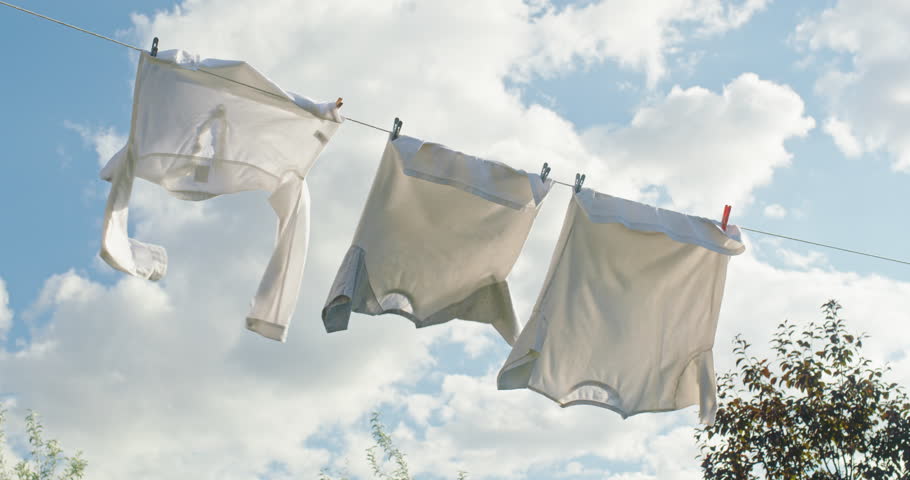Freshly washed white clothes drying on a clothesline in the sunlight against a blue sky with clouds. High quality 4k footage