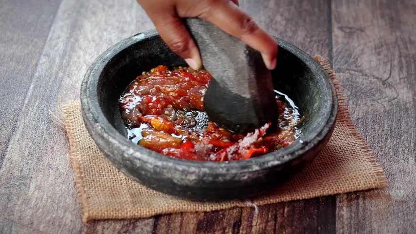 Close up Asian woman hand are grinding chili with stone or manual process of making chili sauce, all the ingredient crushed using stone pestle on stone mortar.