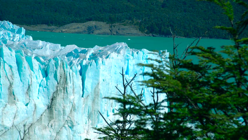 Perito Moreno Glacier in Argentina features towering ice formations against a turquoise lake, surrounded by a forested landscape.