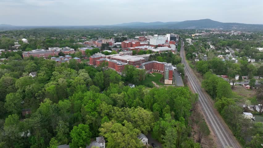 Green trees between red brick University of Virginia during Cloudy day. Railroad tracks in Charlottesville, USA. Aerial wide shot. Historic buildings on campus area.