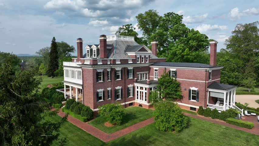 Majestic American mansion with classic brick facade and multiple chimneys, nestled in lush greenery. Elegant architecture with large windows and spacious lawn.Aerial view.