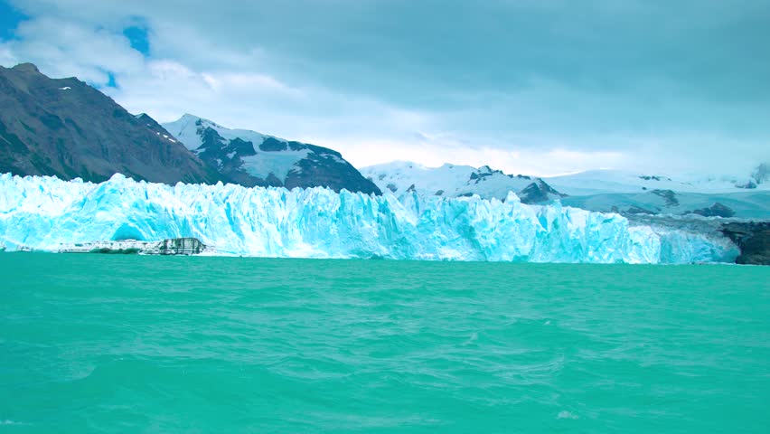 Perito Moreno Glacier in Argentina displays towering ice formations glistening against a turquoise lake, surrounded by rugged mountains and dramatic skies.