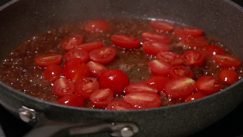 cherry tomatoes cut in half cooking in a pan close up