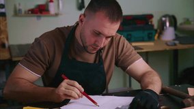 Professional craftsman carefully sketching intricate project details on paper while sitting at wooden workbench inside well organized workshop, demonstrating precise design process - Powered by Shutterstock - Get 15% off with code: PIKWIZARD15