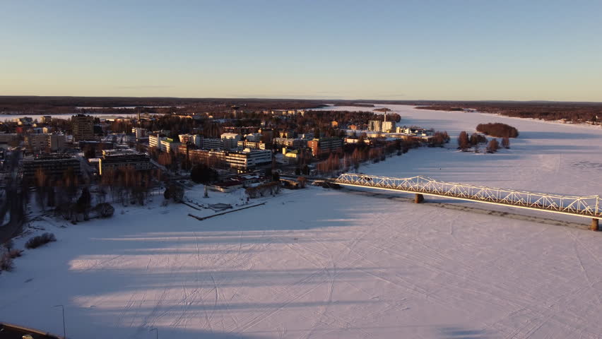 Aerial flying backwards from buildings on banks of frozen Torne River in Tornio, Finland