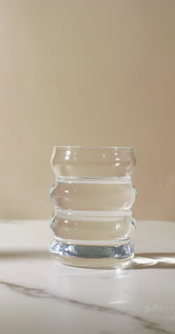 A translucent scoop of fine white powder, possibly creatine, magnesium, or electrolytes, is poured into a clear glass of water, highlighting a clean supplement routine on a marble surface.