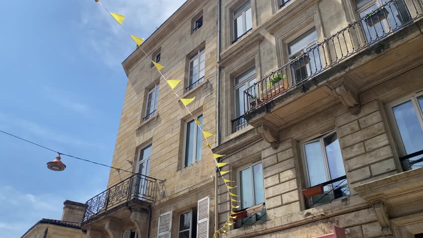 Traditional French residential buildings with shutters and balconies on a narrow sunny street. View from below, bright summer sky above. Bordeaux, France.