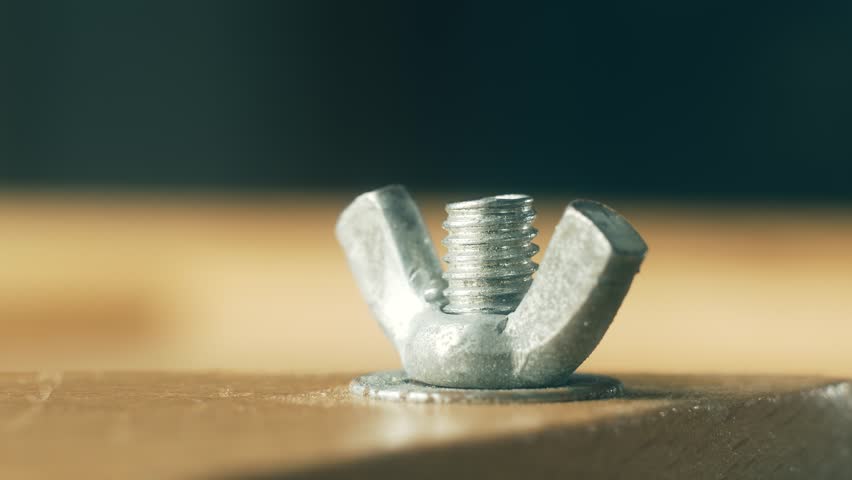 Close-up metal wing nut unscrewing from bolt by man using hands. Macro view hardware fastener loosening manually without tool by repairman. Steel nut turning out by builder with fingers during