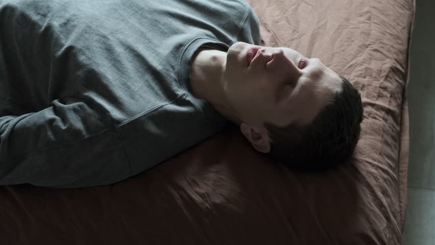 Dramatic man crying in despair. Portrait of emotional man lies on the bed and cries shedding a tear. Eye with tear drop. Depression or existential crisis