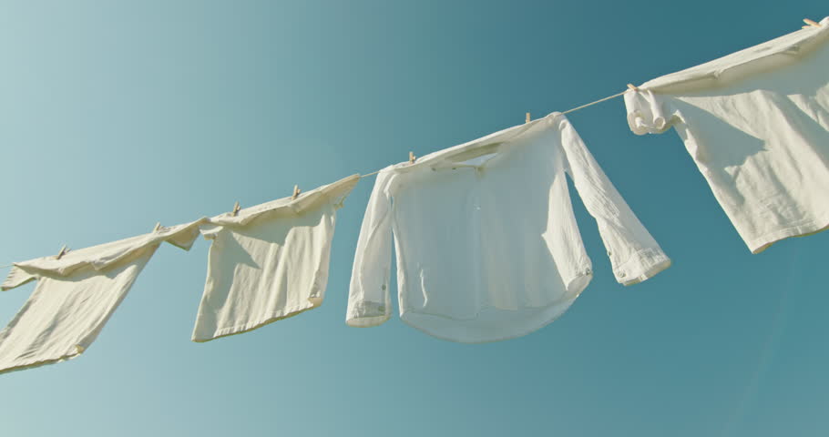 Freshly washed white clothes fluttering in the wind on a clothesline under bright blue sky in sunny weather. High quality 4k footage