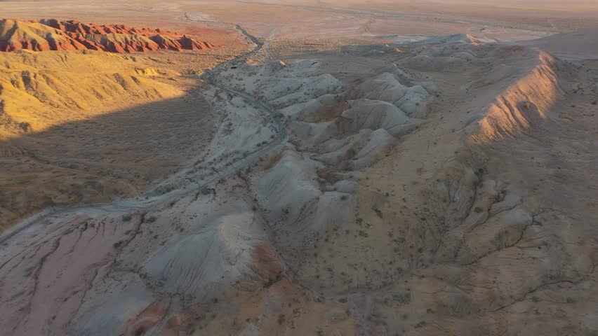 Golden hour illuminating winding desert road cutting through vibrant canyon landscape, revealing dramatic geological formations and expansive wilderness beneath dramatic sky