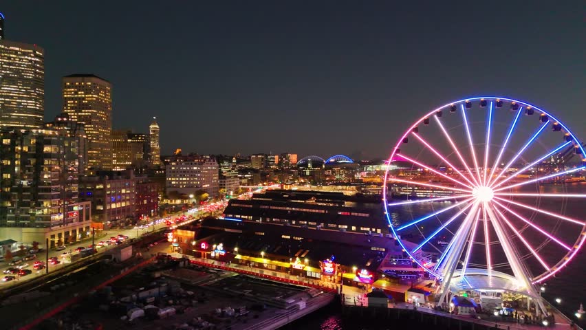 A breathtaking aerial night view of downtown Seattle, Washington, showcasing the illuminated skyline and iconic skyscrapers. Glowing Seattle Great Wheel. Seattle at night. Top cinematic aerial view