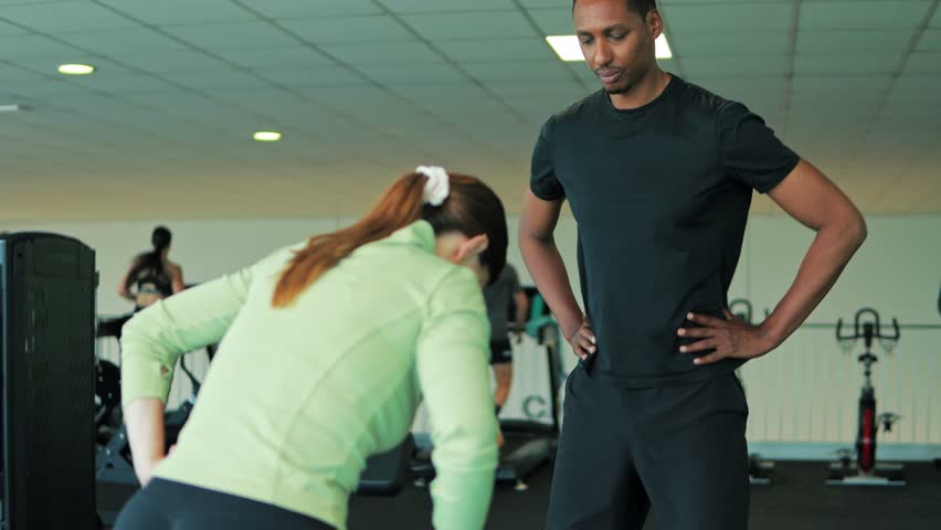 Fitness instructor assisting woman with proper form during workout, emphasizing posture and technique in gym setting with exercise equipment.African american personal trainer at gym .Healthy lifestyle