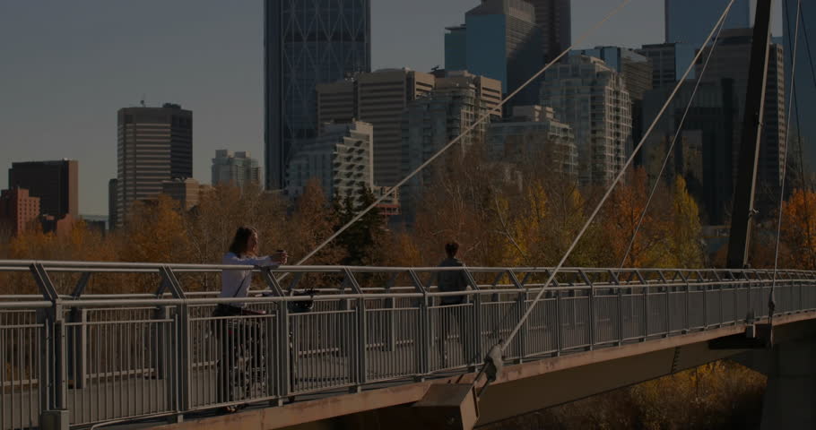 Man leaning on pedestrian bridge railing, viewing finance line graphs floating across city skyline. Urban, technology, modern, finance, skyline, destination, connectivity