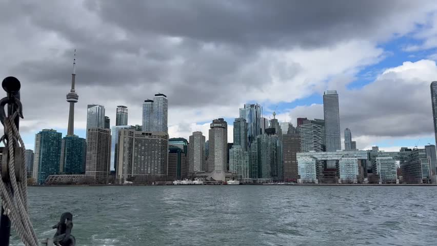 Toronto skyline view from the water with CN Tower and modern buildings under cloudy sky. Shot from a boat on Lake Ontario.