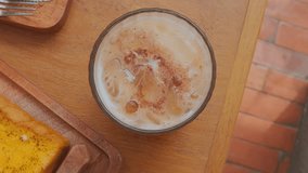 A top view of a glass filled with a frothy beverage, possibly iced coffee or tea, garnished with a sprinkle of cinnamon. The drink has ice cubes and a creamy texture - Powered by Shutterstock - Get 15% off with code: PIKWIZARD15