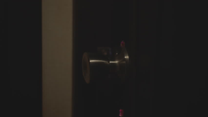 Close up hand in fluffy sweater gripping metal knob and turning door open to enter neon lit studio bathed in pink purple hue as silhouette steps through threshold under moody ambient glow