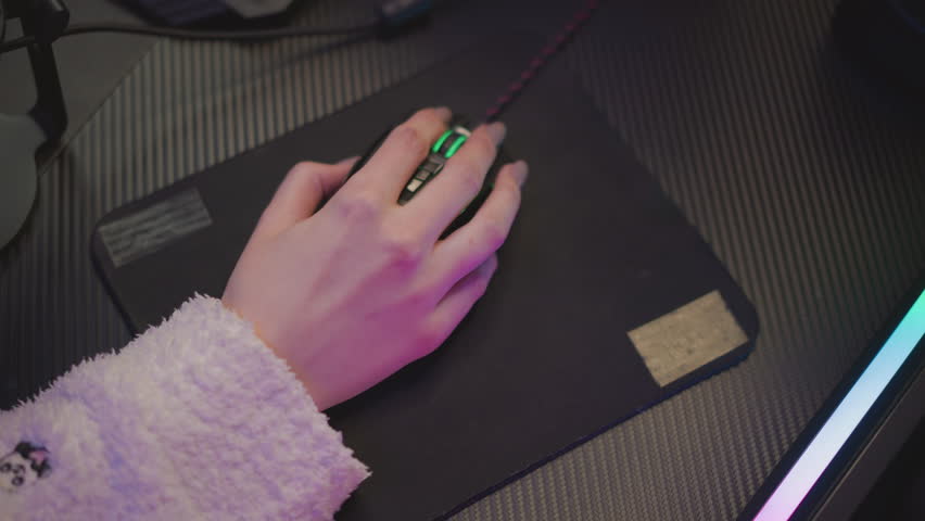 Close up hand of lady in fluffy sweater resting on mouse with green light glowing beneath fingers, placed on black mousepad over dark textured desk, subtle ambient lighting
