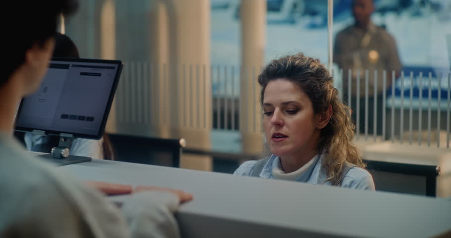 Airport Check-in Counter: Female Airline Check-in Attendant Talking to Passenger, Asking Questions During Passport Check for Boarding Flight. Security Checkpoint in International Airport Terminal.
