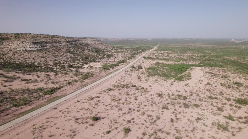 A rural road in the west texas desert with distant 18 wheelers