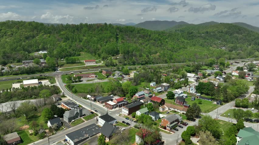 Calm green trees in small american village with traffic on interstate leading between mountains. Aerial wide shot. Historic small town in Virginia, USA. Panorama aerial view.