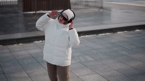 Energetic young lady wearing white winter jacket, dark glasses and headset dances on paved park plaza with snowbanks and trees under soft winter daylight, expressing freedom with dynamic moves - Powered by Shutterstock - Get 15% off with code: PIKWIZARD15
