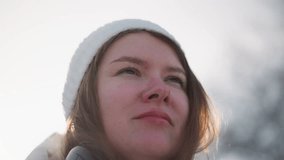 Close up shot young woman adjusting dark visor goggles over white beanie while smiling under bright winter sun with wind tousling hair and blurred snowy downtown urban background - Powered by Shutterstock - Get 15% off with code: PIKWIZARD15