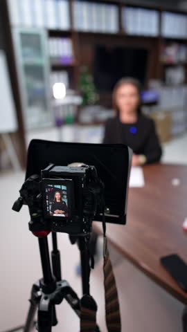 Professional camera with display filming a Caucasian brunette sitting at desk. Close up. Creation of content for internet blog. Vertical video.