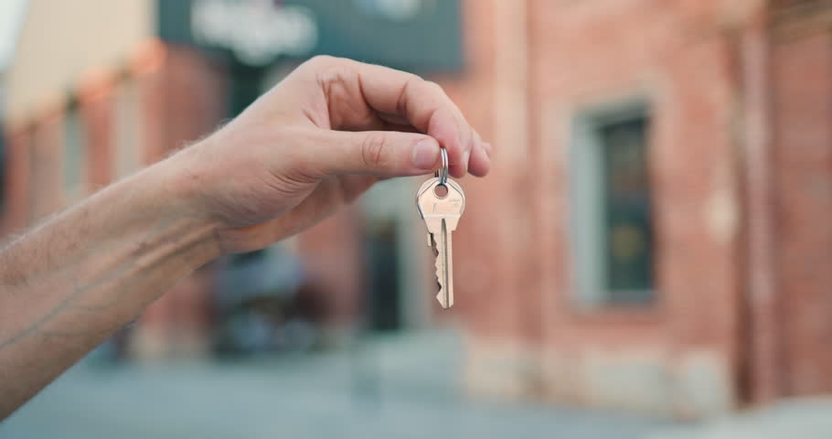 Close-up hand holding key from a new house outdoor.