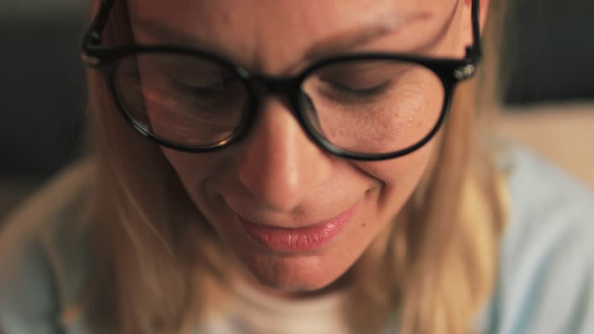 Young professional woman wearing eyeglasses closely examining bitcoin gold coin, verifying authenticity with playful, curious expression while exploring cryptocurrency investment potential.