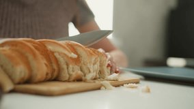 Close up of chef slicing loaf of bread with knife on wooden board focus on serrated blade cutting through crust into even slices with crumbs falling on white table under soft window light in kitchen - Powered by Shutterstock - Get 15% off with code: PIKWIZARD15