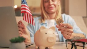 Woman hold small united states flag and golden bitcoin near piggy bank while sitting at table with laptop, representing cryptocurrency investment and financial planning with optimistic attitude. - Powered by Shutterstock - Get 15% off with code: PIKWIZARD15