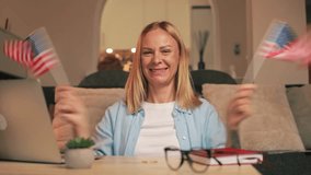 Enthusiastic woman waving two small american flags while sitting at table with laptop, glasses and notebook, expressing patriotism and excitement.USA celebrate 4th of July. Independence Day concept - Powered by Shutterstock - Get 15% off with code: PIKWIZARD15