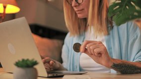 Confident businesswoman analyzing cryptocurrency investment on laptop, holding bitcoin coin with optimistic smile while working at desk during evening hours.Cryptocurrency investment concept. - Powered by Shutterstock - Get 15% off with code: PIKWIZARD15