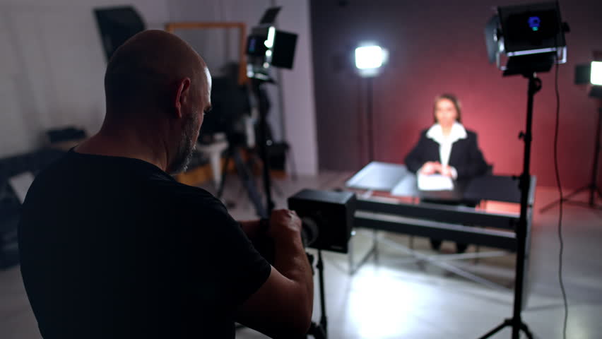 Mature man in black t-shirt stands at camera. Cameraman recording a video with female blogger.