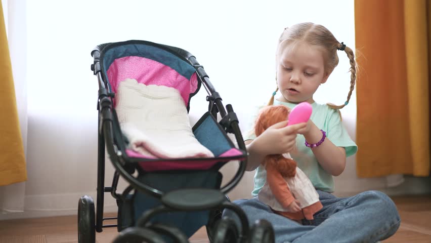 Little girl sitting in stroller with doll. Girl plays with a stroller and doll toys. Family playing in the backyard at home. A small girl in a stroller holding a lifestyle.
