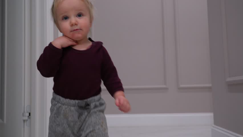 A child toddles through a modern, minimalist home interior with soft hues and an open doorway