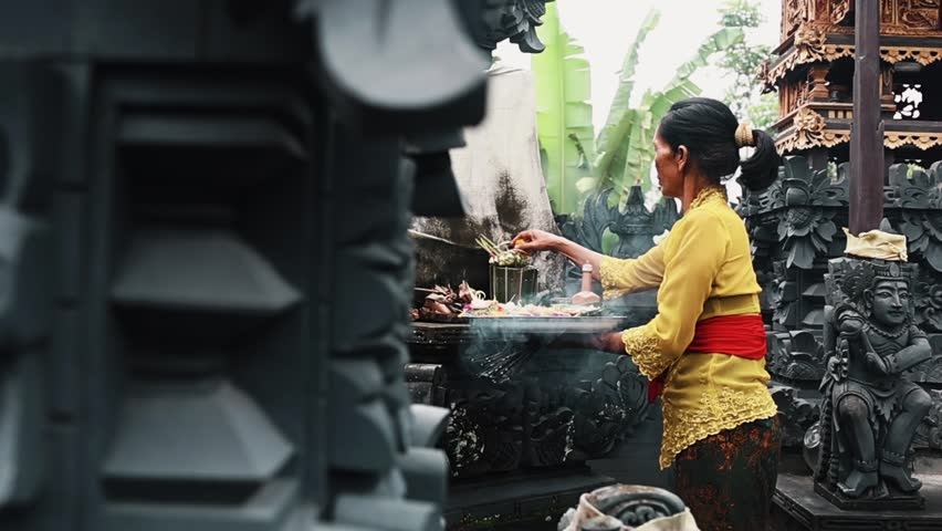 A Balinese woman performing traditional offering rituals at a scenic temple setting