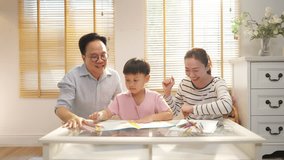 Happy Asian family parents teaching little child boy do homework in living room. Father, mother and son enjoy spending time together at home. Family relationship, homeschool and preschool education. - Powered by Shutterstock - Get 15% off with code: PIKWIZARD15