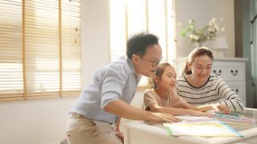Happy Asian family parents teaching little child girl do homework in living room. Father, mother and daughter spending time together at home. Family relationship, homeschool and primary education. - Powered by Shutterstock - Get 15% off with code: PIKWIZARD15