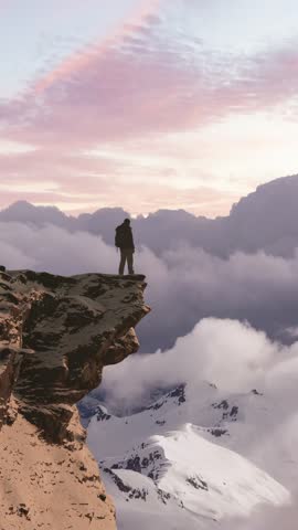 Hiker on a Cliff Edge Overlooking Snowy Mountain Peaks at Sunset