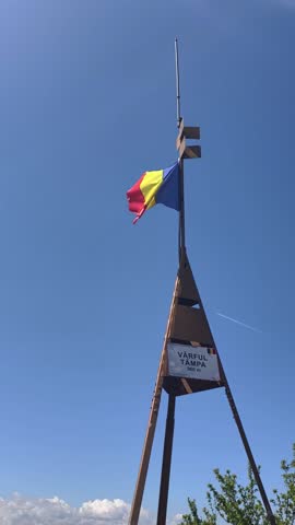 Romanian flag waving at the summit of Tâmpa Mountain (Vârful Tâmpa) at 960 meters above sea level, above Brașov, Romania. The metal structure marks the peak and proudly displays the national colors 