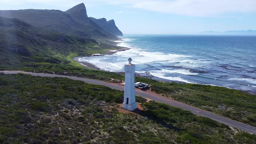 a scenic aerial view with a white lighthouse, mountains, and ocean on a bright and sunny day at the coast south africa