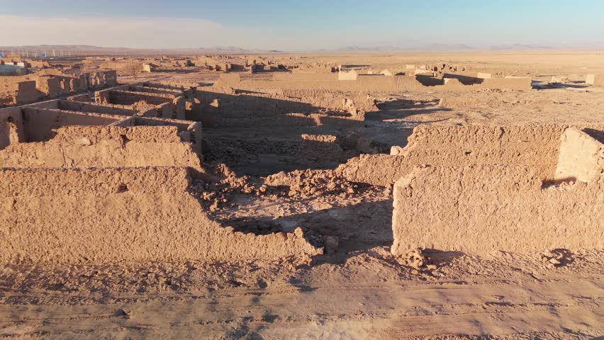 Close-up drone shot of the ruined adobe facades of a former saltpeter works, close flight moving forward into the sunset in the desert