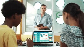 Smart teacher hold tablet while back view student learning engineering code on table with laptop and electronic equipment scatter around. Happy children working together to write program. Edification - Powered by Shutterstock - Get 15% off with code: PIKWIZARD15