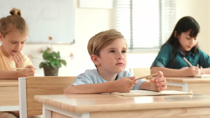 Caucasian boy raising hand for asking and answering teacher surrounded by diverse children studying at classroom. Happy student working together, voting, volunteering, calling instructor. Pedagogy. - Powered by Shutterstock - Get 15% off with code: PIKWIZARD15
