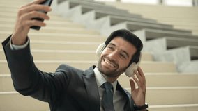 Smiling business man listening music while looking at mobile phone. Project manager holding phone while enjoy hip-hop song at stairs. Caucasian leader listen relax sound while plan project. Exultant. - Powered by Shutterstock - Get 15% off with code: PIKWIZARD15