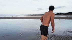Barefoot man in swim trunks misses a frisbee across shallow tidewater on Omaha Beach, with Normandy’s green coastline and coastal homes in the background, captured in slow motion - Powered by Shutterstock - Get 15% off with code: PIKWIZARD15